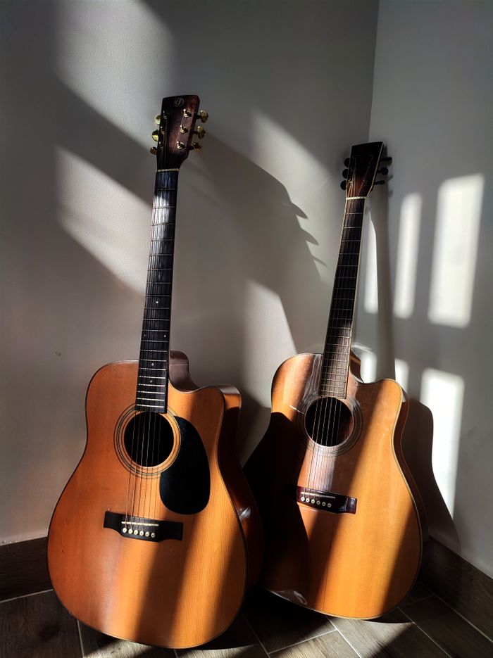 Home Two classic wooden acoustic guitars with shadows on a wall, creating a vintage vibe.