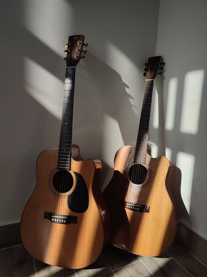 Services Two acoustic guitars standing against a white wall, casting dramatic shadows in sunlight.